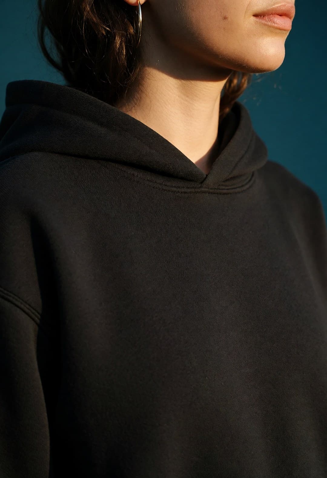 Close crop of a gold hoop earring and dark hair against a black fleece hood