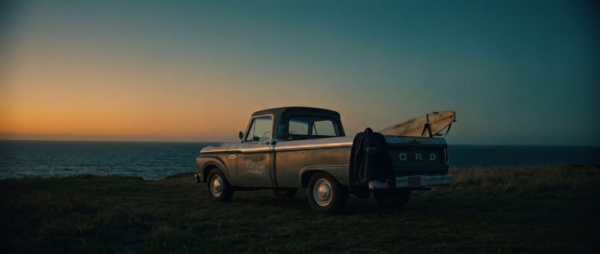 An empty coastline at last light, a truck parked facing the water
